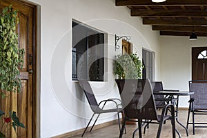 Veranda with chairs and table on the wooden floor. Front facade with door and windows and plants