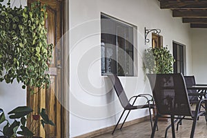 Veranda with chairs and table on the wooden floor. Front facade with door and windows and plants