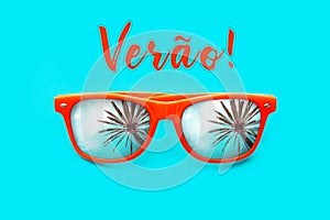 Verao text in Portuguese: Summer and orange sunglasses with palm tree reflections isolated in cyan background.