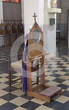 Verical view of a confessional chair and kneeler bench inside a church in southern India