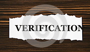 VERIFICATION - word on a white tattered piece of paper on a wooden background