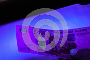 verifying the authenticity of money in ultraviolet light. 5000 rubles paper currency of Russia under ultraviolet light