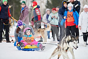 Little kid on snow tubing with sled dog