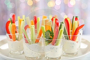 Verrines appetizer with carrot, cucumber, celery and red bell pepper sticks in glasses on platter at bokeh background,