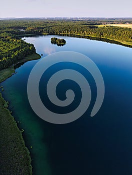 Vertical aerial of a picturesque lake surrounded by forests with leafy trees