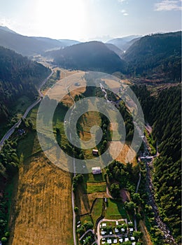 Vertical aerial view of a camping and harvested field, parking for a camper van, sunrise summer, mountains and a river near the