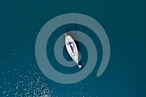 Vertical aerial view of an isolated boat floating on the water of a greenish colored lake, docked to a buoy