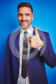 Vertical angle picture of young handsome business man over blue isolated background doing happy thumbs up gesture with hand