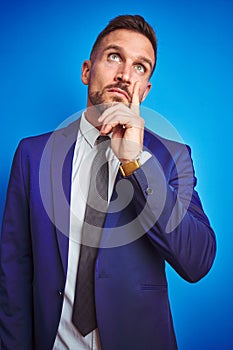 Vertical angle picture of young handsome business man over blue isolated background with hand on chin thinking about question,