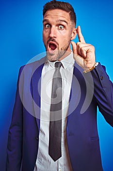 Vertical angle picture of young handsome business man over blue isolated background pointing finger up with successful idea