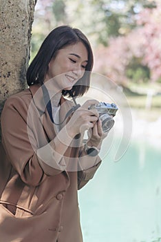 Vertical Asian Women with vintage film camera take a photo. Smiling female photographer look at photo from professional camera