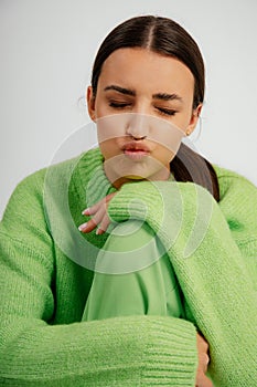 Vertical attractive brunette woman in green costume with close eyes, putting lips in tubule and leaning on knee by hands