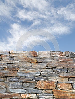 Vertical background with rough stone wall and blue cloudy sky