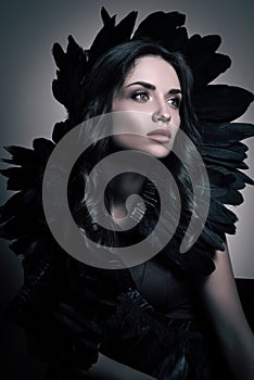 Vertical beauty portrait in dark tones. Luxury young woman with black feathers in her hair