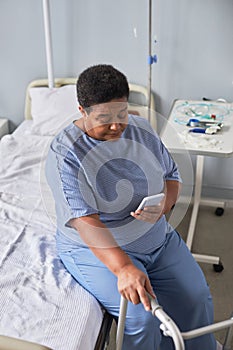 Vertical black senior woman using mobile phone in hospital room