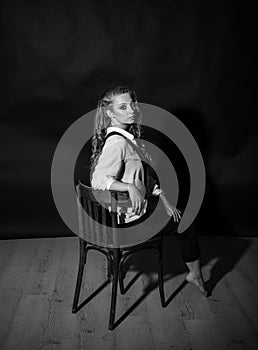 Vertical black and white portrait of a pretty barefoot blonde sitting on a chair in the studio