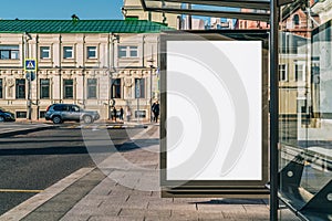 Vertical blank billboard at bus stop on city street. In background buildings, road. Mock up. Poster next to roadway.