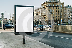 Vertical blank glowing billboard on the city street. In the background buildings and road with cars. Mock up.