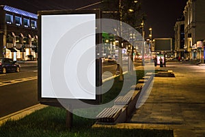 Vertical blank glowing billboard on night city street. In background buildings and road with cars. Mock up.