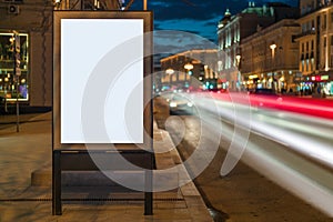 Vertical blank glowing billboard on night city street. In background buildings and road with cars. Mock up.