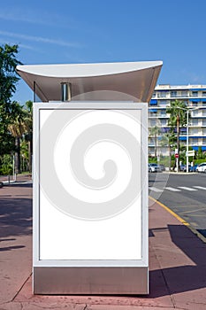 Vertical blank white billboard at bus stop on city street. In the background buildings and road. Mock up. Poster on street