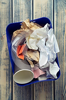 Vertical blue plastic container box full of waste, rubbish on wooden background. Sustainable development, recycling