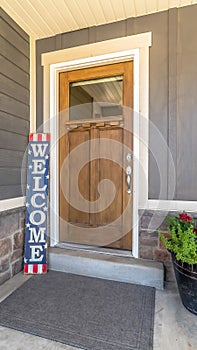 Vertical Brown front door with glass pane and Welcome sign against gray and stone wall