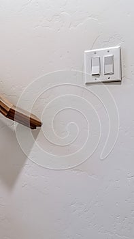 Vertical Brown wood handrail of staircase and rocker light switch against interior wall