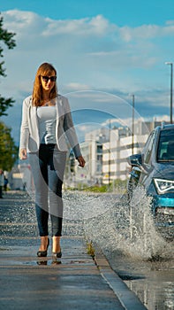 VERTICAL: Businesswoman walking along sidewalk gets splashed by careless driver