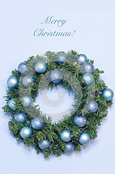 Vertical card with Christmas winter wreath on the door of fir branches with balls on blue background on New Year`s Eve.