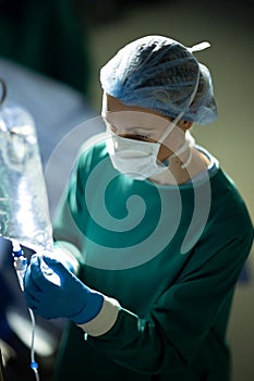 Vertical of caucasian female surgical tech preparing iv bag in operating theatre during opertion