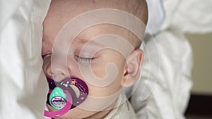 Vertical close-up face newborn chubby sleeping baby lying on stomach open eyes and smile covered with blanket on bed on