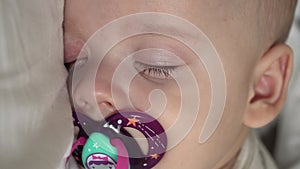 Vertical close-up face newborn chubby sleeping baby lying on stomach open eyes and smile covered with blanket on bed on