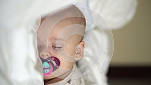 Vertical close-up face newborn chubby sleeping baby lying on stomach open eyes and smile covered with blanket on bed on