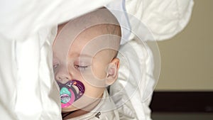 Vertical close-up face newborn chubby sleeping baby lying on stomach open eyes and smile covered with blanket on bed on