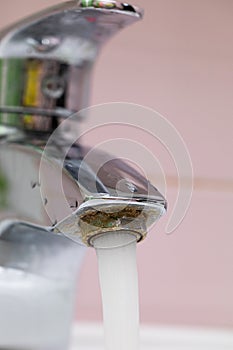 Vertical close up flowing tap water on pink tiled background. Faucet water from rusty spigot. Plumbing, house appliance