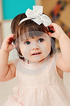 Vertical close up indoor portrait of cute happy baby girl playing with dressy white headband