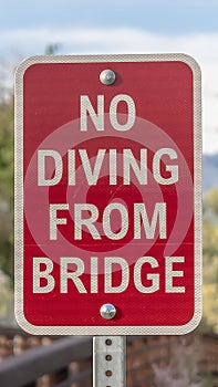 Vertical Close up of a No Diving sign beside a bridge with brown metal guardrail
