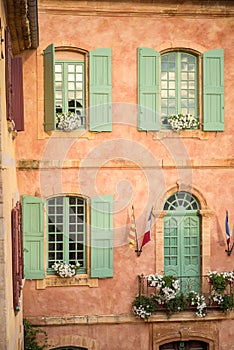 Vertical close-up picture of town hall in Roussillion, Provence, France. Old historical building with orange walls and green