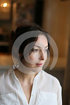 Vertical close-up portrait of a beautiful brunette in a white blouse on a background of home interior
