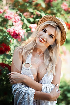 Vertical close-up portrait of beautiful sexy tanned blonde girl in white swimming suit, pareo and straw hat looking in camera.