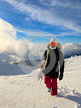 CLOSE UP Smiling young woman hikes up an ungroomed hill during snowboarding trip photo