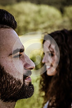 Vertical close up of a profile view of a smiling bearded man`s face in the foreground and a smiling woman`s face in profile in t