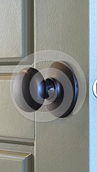 Vertical Close up of a round black door knob installed on a gray paneled interior door