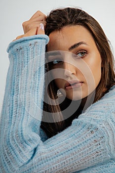 Vertical close up sad serious dark haired woman looking away and biting lips in blue woolen oversize sweater in studio
