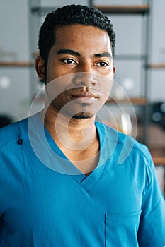 Vertical close-up shot of handsome African American male doctor wearing blue surgeon medical uniform standing in