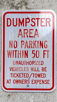 Vertical Close up of a sign that reads Dumpster Area No Parking against a concrete wall