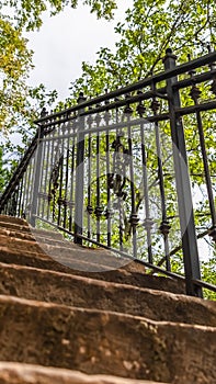 Vertical Close up of staircase with stone treads and metal railing against leaves and sky