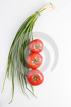 Vertical close up top view shot of a bunch of green onions and three ripe red tomato on a white background