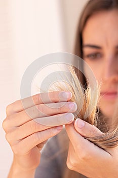 Vertical close up view of frustated cropped young woman looking and touching her blond damage hair selective focus
